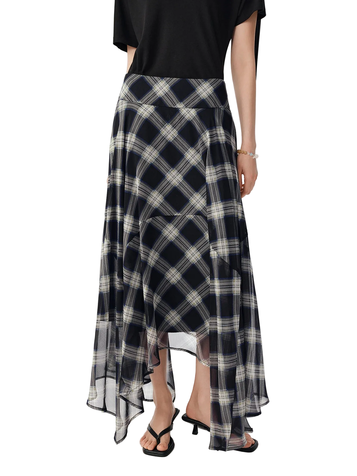 A model from the waist down wearing a black, white, and gray plaid high-low skirt with a sheer overlay, paired with a black top and black sandals. The brand name 'Dushu' is visible in the top left corner.