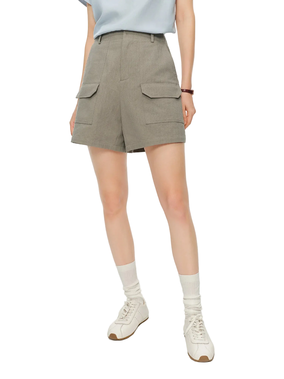 A model wearing high-waisted, light gray cargo shorts with flap pockets, styled with a light blue top, white socks, and white sneakers against a plain white studio background.